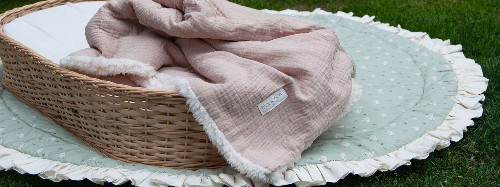 Wicker crib with pink blanket on a green grass background